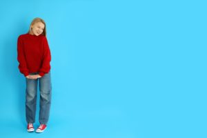 Attractive girl in sweater, jeans and sneakers on blue background